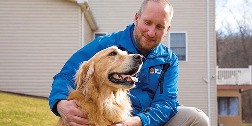 Man with blue jacket petting a Golden Retriever outside. 